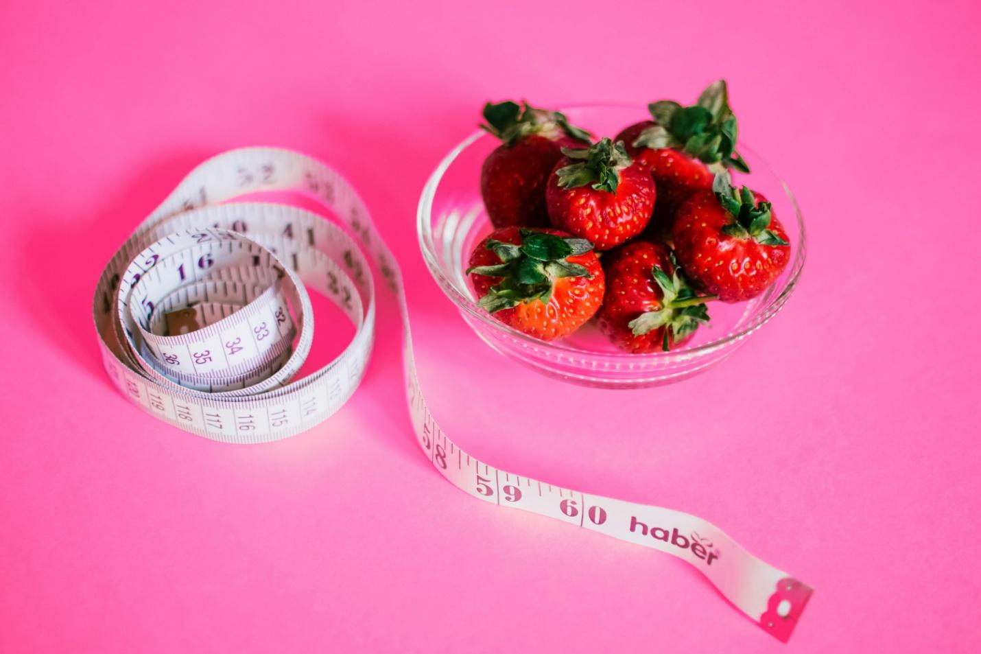 A picture of strawberries and a measuring tape against a pink surface